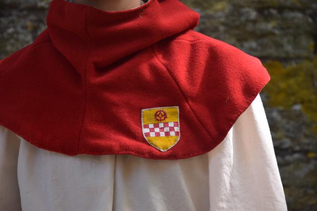Auf der Gugel aufgenäht ist das Kamener Stadtwappen, das Wappen der Grafschaft Mark (rot-weißer Schachbalken auf goldenem Grund) mit dem Kamener Kammrad als Schildhaupt.

Ob es ein Mühlrad oder ein anderes, evtl. ein germanisches Sonnenrad darstellt ist undklar - vieles spricht aber nach heutigem Stand für ein Mühlrad, da es eine Mühle an der Seseke direkt vor der Stadt gab.