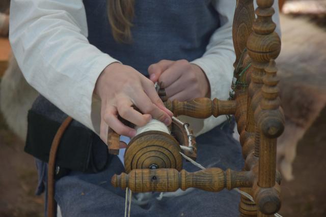Berenike kontrolliert das Garn am Spinnrad.
