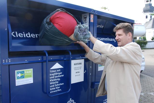 Manfred Küppers, der Küster der evangelischen Kirchengemeinde Alpen zeigt, wie man die Säcke mit nicht mehr benötigter Kleidung in einen der beiden Container in der Nähe des Gemeindehauses wirft.