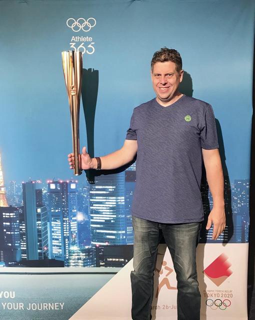 Jörn Becker vor der Imagewand mit der Fackel für Olympia 2020.