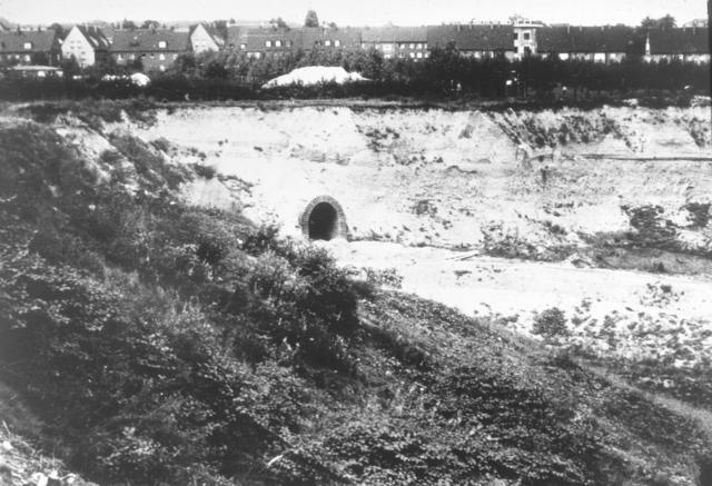 Dieses historische Bild zeigt einen der Bunkerzugänge von der Tongrube aus. Die Tongrube, heute ein Biotop, gehörte zur Ringofen-Ziegelei die sich bis in die 1960-Jahre an der Evinger Straße befand. Am oberen Rand des Fotos sind Häuser an der Probstheidastraße zu erkennen.