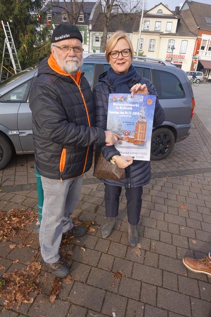 Günter Kalla und Monika Fontaine - zwei der drei Organisatoren des Richrather Weihnachtsmarktes - zeigen das Plakat des Weihnachtsmarktes.