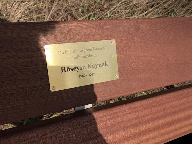 Auf einer Plakette, die an der Rückenlehne der Sitzseite angebracht ist, steht geschrieben: „Du bist in unserem Herzen – Kalbimizdesin“ - Hüseyin Kaynak - 1960 bis 2019.