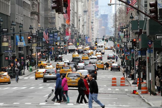 Wolkenkratzer, viele Menschen, Taxis, Schilder und Fahnen. Ein typischer Anblick in Manhattan.