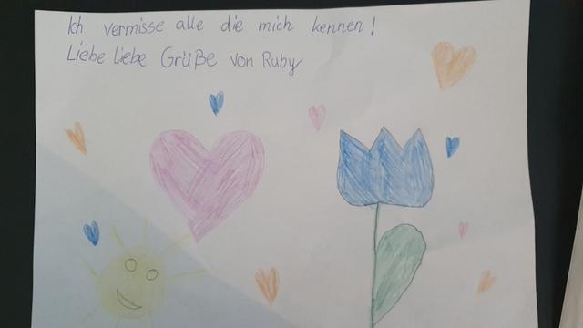 Einen Gruß mit Blume, Herzen und Sonne sendet Ruby (neun Jahre) an alle, die sie kennen.