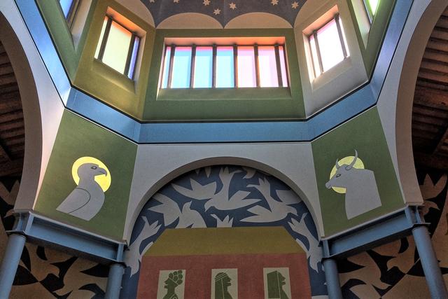 Lichtkuppel mit stilisierten Tauben , Symbol des Hl. Geistes, Patrozinium der Kirche. Stier und Adler sind Symbole für die Evangelisten Lukas und Johannes. Unter dem Dach werden Menschen unterschiedlicher Herkunft und Religion empfangen. In den Fenstern des Hauses Gottes erscheinen exemplarisch ein Jude, ein Moslem und eine Christin.
