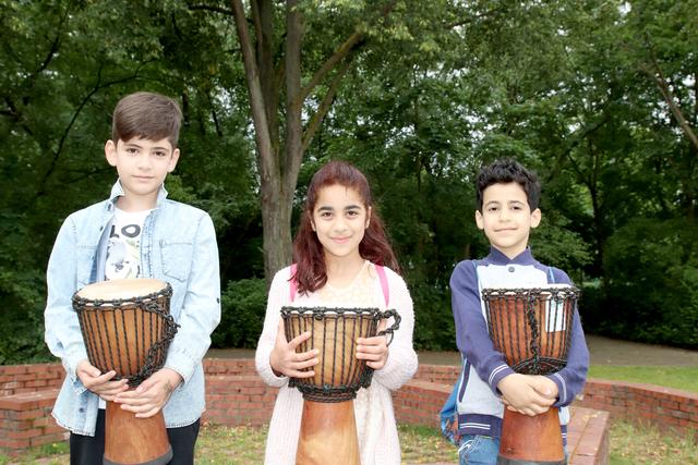 Mit ihren Schulsozialarbeitern lernen Joud, Nour und Zen die richtige Technik auf der Djembe-Trommel (v.l.n.r.)