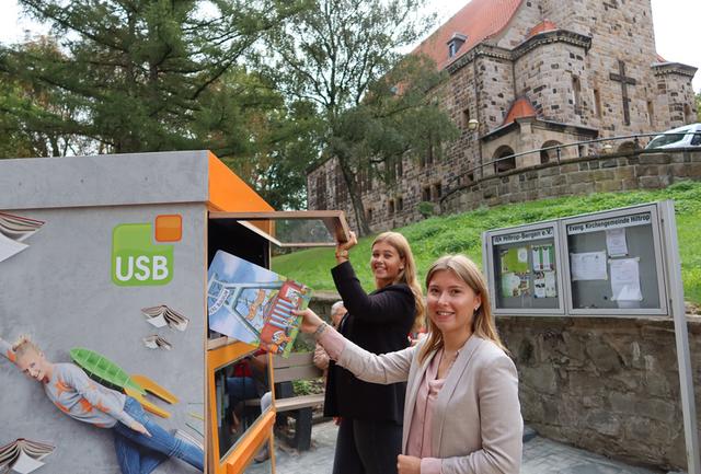 Die Auszubildenden Laura Budzinski und Nadine Wolny befüllen den neuen Bücherschrank vor der Hiltroper Kirche.