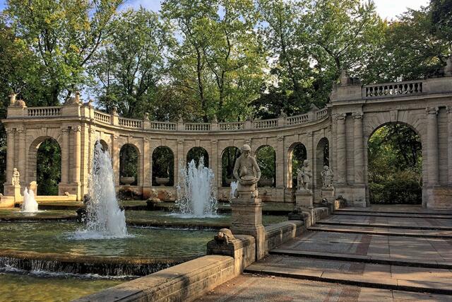Arkaden, Märchenfiguren und Tiere gehören zur Gestaltung des Brunnens. Im leicht abschüssigen Gelände fließt das Wasser in vier Kaskaden in das untere Becken.
