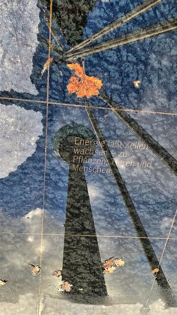 Im Steinfundament der Energiepyramide  spiegeln sich Rheinturm und Pyramidenschenkel im Regenwasser.   | Foto: © Margot Klütsch