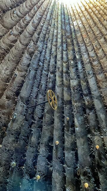 Die Verschalung mit Fichtenstämmen ist gut erkennbar. In die Wand sind keine Glasöffnungen eingelassen. Neben der großen Öffnung an der Spitze spenden sie gedämpftes Licht. Das Rad ist das Meditationszeichen von Bruder Klaus.  | Foto: ©Margot Klütsch