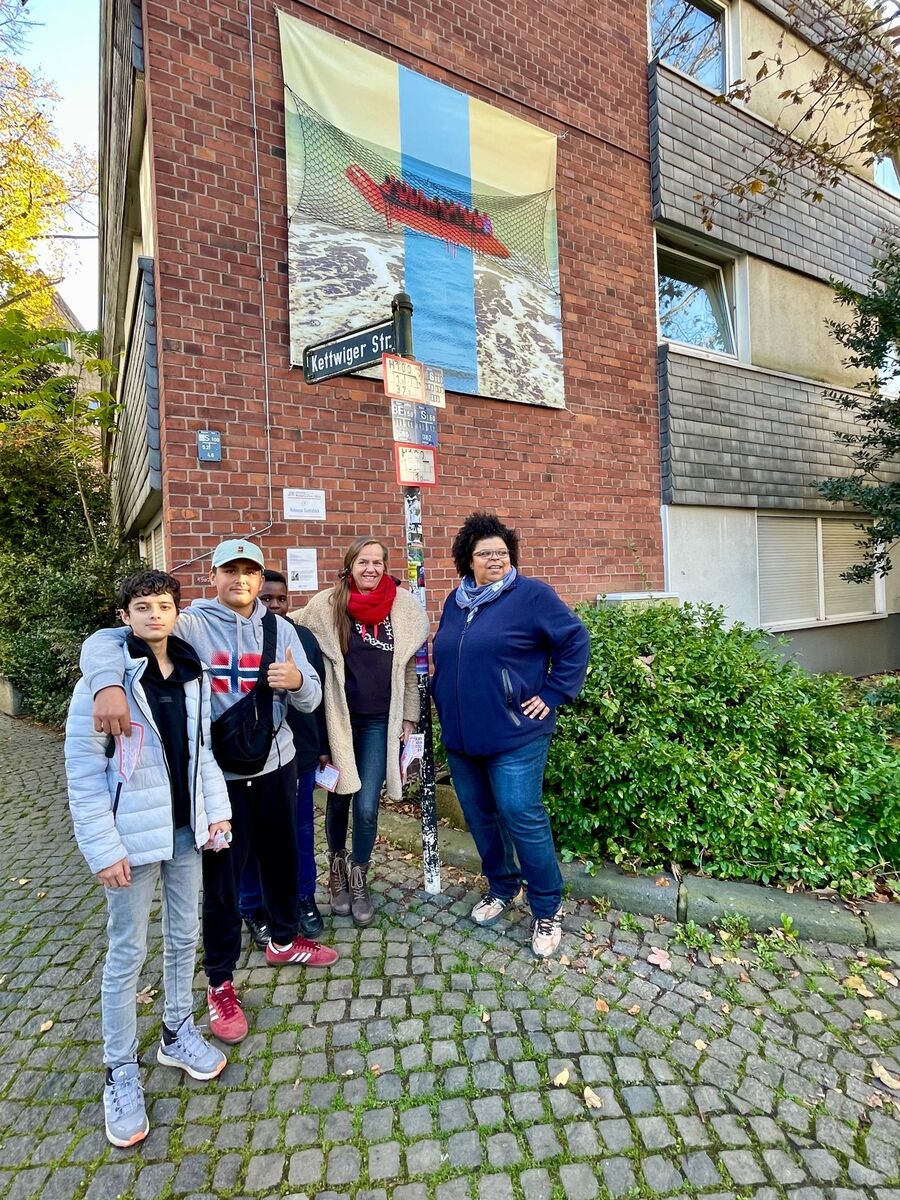 Rebecca Gottschick (re.) mit Besuchern vor ihrem Werk "Die Duldung oder ich bin hier nicht erwünscht."

Ich sitze im Boot.
Das Ufer ist in Sicht.
Die Lichter glitzern.
Es gibt Nahrung, Kleidung.
Es ist Platz für alle: es muss das Paradies sein!
Nur leider ist es das nicht.
Die Realität ist eine andere:
Es könnte das Paradies sein, ein Netz der Sicherheit.
Wenn man willkommen ist und einen einfachen Weg dorthin hätte.
Wer es an das Ufer schafft wird geduldet ist aber noch lange nicht erwünscht.
Das ganze findet nicht nur auf dem Meer statt.
Nein. Auch direkt vor unserer Haustür.

Ich bin geduldet. Ich bin hier nicht erwünscht. | Foto: Mülheimer Kunstverein KKRR