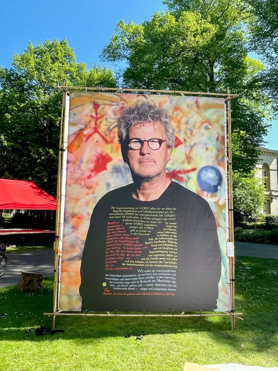 Auf diesem Plakat mit Großfoto von Gründungsmitglied ArtObscura Gert Rudolph ist zu lesen:
"Wir wollen die Unterschiedlichkeit von Menschen präsentieren, sie mit ihrem Sein anerkennen und wertschätzen und damit einen Raum schaffen, in dem Menschen, die normalerweise nicht im Blickpunkt der Öffenlichkeit oder eher "am Rand" stehen, sich . immer abstrahiert über die künstlerische Ebene - zeigen und präsentieren können.
Gert Rudolph, 63 Jahre alt, geboren und wohnhaft in Mülheim an der Ruhr" | Foto: Mülheimer Kunstverein KKRR, Delle 54-60