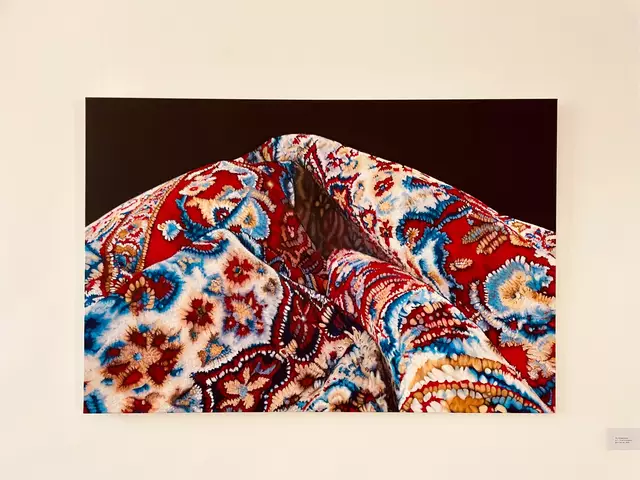 Feinste Ölmalerei - von Pia Winkenstern in der Ruhr Gallery  - eigentlich O.T. aber im Zusammenhang mit dem Irankonflikt auf besondere Weise aktuell - was verbirgt sich hinter dem schönen Schein des Orientteppichs?
Dieses Werk greift das Motiv des Perserteppichs auf und spielt offenbar mit Form, Textur und kultureller Symbolik. Der Teppich ist nicht einfach als Bodenobjekt dargestellt, sondern als kunstvoll drapierter, fast skulpturaler Stoff. Das hat mehrere denkbare Bedeutungen:

1. Ästhetische Hommage
Die Malerin zeigt die visuelle Komplexität und Schönheit persischer Teppichmuster.

Die Detailtreue ehrt die Handwerkskunst dieser traditionellen Textilien.

2. Abstraktion oder Transformation
Durch die Vergrößerung und das Fehlen eines klaren Kontexts wird das Objekt abstrahiert.

Der Teppich wird zur Landschaft, Skulptur oder fast zum Körper – das kann den Betrachter irritieren oder faszinieren. Soll er - so aufgerollt und geknickt - etwa entsorgt werden - weil nicht mehr zeitgemäß?

3. Kulturelle Referenz
Perserteppiche sind Symbole für Kultur, Geschichte und Identität des Iran.

In einem westlichen Ausstellungskontext können sie Fragen nach Orientalismus, Aneignung, Globalisierung oder Nostalgie oder Wechsel aufwerfen. | Foto: Mülheimer Kunstverein KKRR / VG Bild-Kunst, Bonn