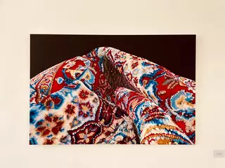 Feinste Ölmalerei - von Pia Winkenstern in der Ruhr Gallery  - eigentlich O.T. aber im Zusammenhang mit dem Irankonflikt auf besondere Weise aktuell - was verbirgt sich hinter dem schönen Schein des Orientteppichs?
Dieses Werk greift das Motiv des Perserteppichs auf und spielt offenbar mit Form, Textur und kultureller Symbolik. Der Teppich ist nicht einfach als Bodenobjekt dargestellt, sondern als kunstvoll drapierter, fast skulpturaler Stoff. Das hat mehrere denkbare Bedeutungen:

1. Ästhetische Hommage
Die Malerin zeigt die visuelle Komplexität und Schönheit persischer Teppichmuster.

Die Detailtreue ehrt die Handwerkskunst dieser traditionellen Textilien.

2. Abstraktion oder Transformation
Durch die Vergrößerung und das Fehlen eines klaren Kontexts wird das Objekt abstrahiert.

Der Teppich wird zur Landschaft, Skulptur oder fast zum Körper – das kann den Betrachter irritieren oder faszinieren. Soll er - so aufgerollt und geknickt - etwa entsorgt werden - weil nicht mehr zeitgemäß?

3. Kulturelle Referenz
Perserteppiche sind Symbole für Kultur, Geschichte und Identität des Iran.

In einem westlichen Ausstellungskontext können sie Fragen nach Orientalismus, Aneignung, Globalisierung oder Nostalgie oder Wechsel aufwerfen. | Foto: Mülheimer Kunstverein KKRR / VG Bild-Kunst, Bonn