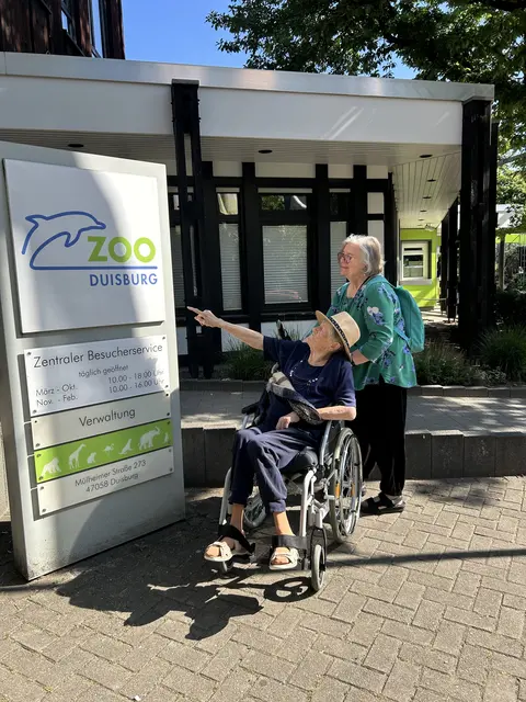 Schon am Zoo-Eingang hat sich Margot Hölbe zusammen mit der ehrenamtlichen Begleiterin Waltraud Baus aufmerksam durchgelesen, was sie denn so alles erwarten könnte.
Foto: Hospizbewegung Hamborn
