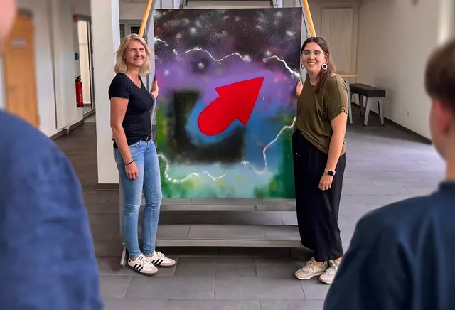Ein Graffiti-Kunstwerk im Polizeipräsidium: Claudia Keßler (l.) und Eileen Just von der Initiative Kurve Kriegen präsentieren die bunte Leinwand, Workshop-Leiter Manuel Meller steht zusammen mit dem jungen Künstler im Vordergrund. Der Kurve-Kriegen-Teilnehmer ist aus Gründen der Anonymisierung bewusst unkenntlich gemacht worden | Foto: Polizei Bochum