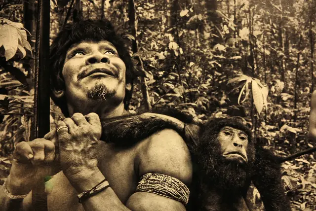 Awá mit einem Affen, den er gerade mit einem Bogen erlegt hat.