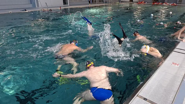 Das Spiel vom Beckenrand betrachtet: Einige Sportler tauchen, einige beobachten das Spiel von der Wasserfläche aus, weitere machen sich im Hintergrund bereit zum Einwechseln. | Foto: Gerling