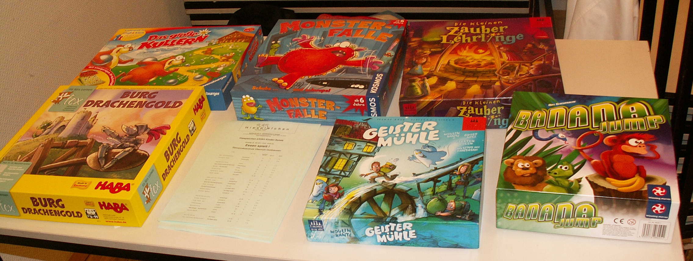 Die Deckel der aufgebauten Spiele: "Das große Kullern" (Ravensburger), "Monster-Falle" (KOSMOS), "Die kleinen Zauberlehrlinge" (Drei Magier Spiele), "Burg Drachengold" (HABA); "Geistermühle" (Drei Magier Spiele); "Banana Jump" (Winning Moves)